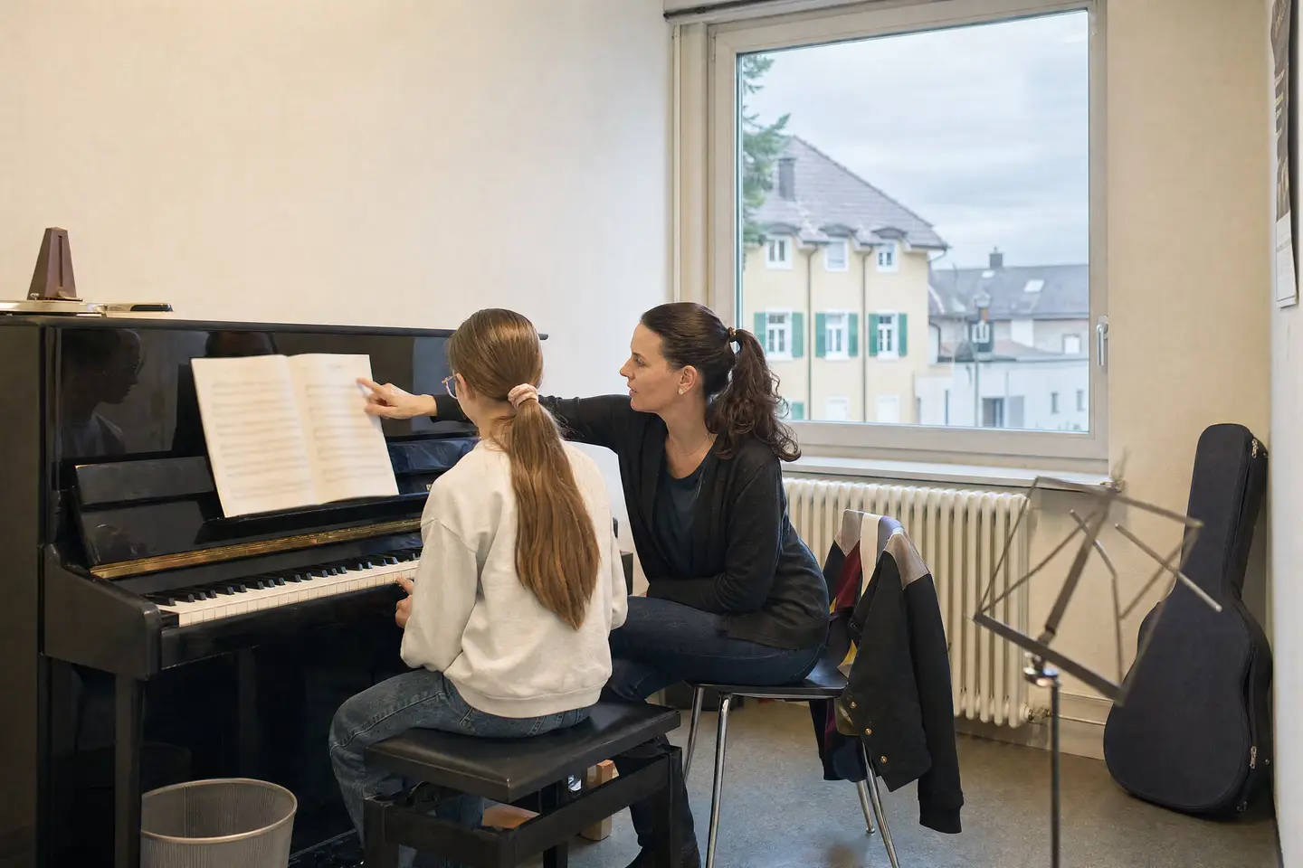 Klavierstunde in einer Musikschule: Schülerin am Klavier, die Lehrerin zeigt auf die Noten