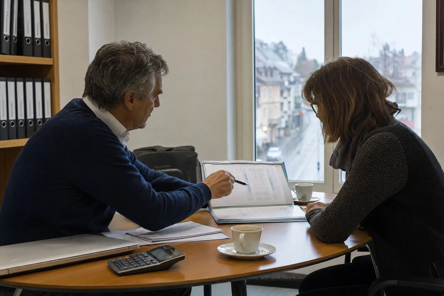 Besprechung am runden Tisch im Treuhandbüro, ein Berater zeigt mit dem Stift auf ein Dokument im Ordner