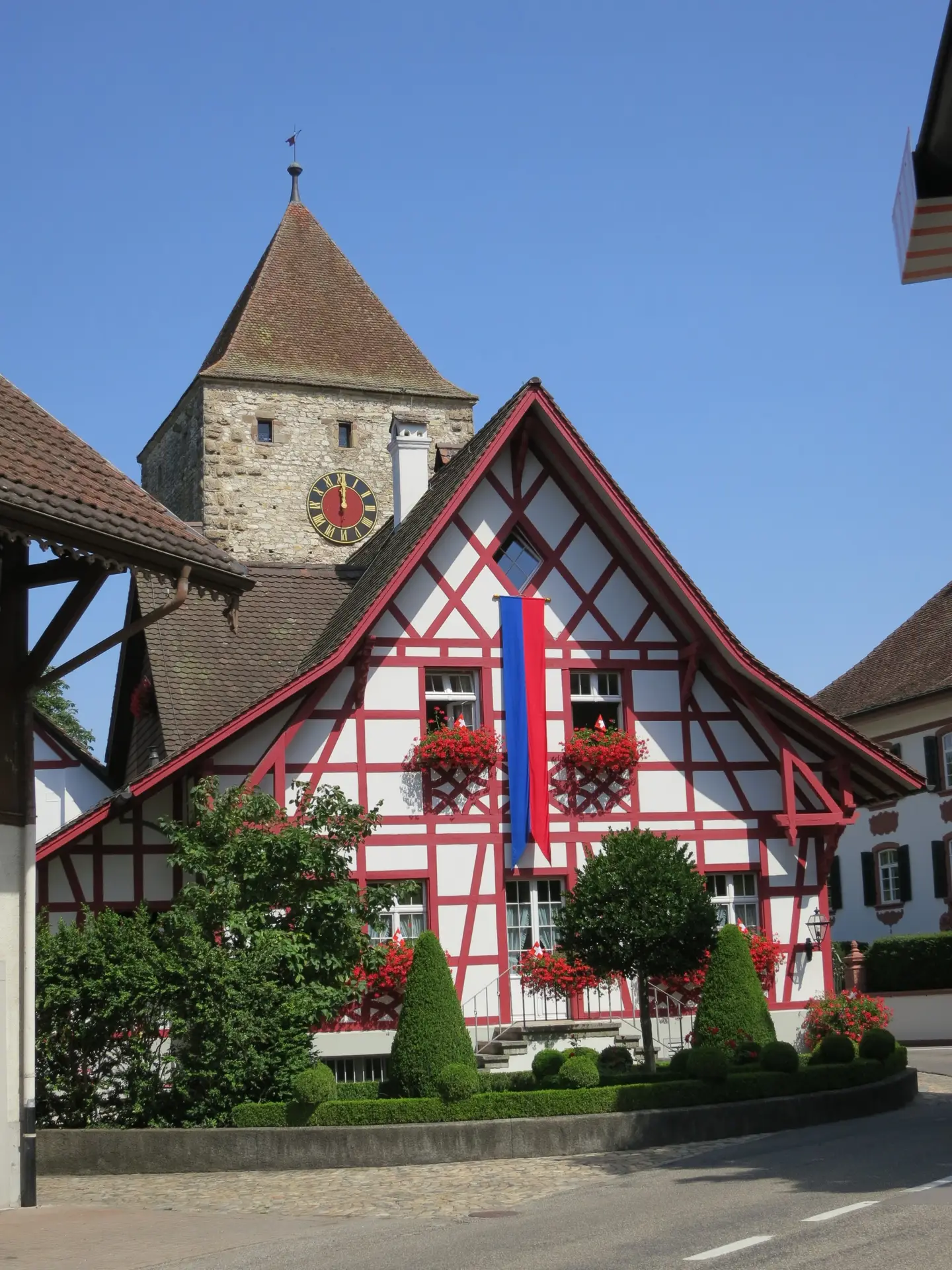 Rot-weisses Fachwerkhaus mit Blumen und Fahne in der Altstadt von Kaiserstuhl, dahinter der Obere Turm aus dem 13. Jahrhundert mit Uhr