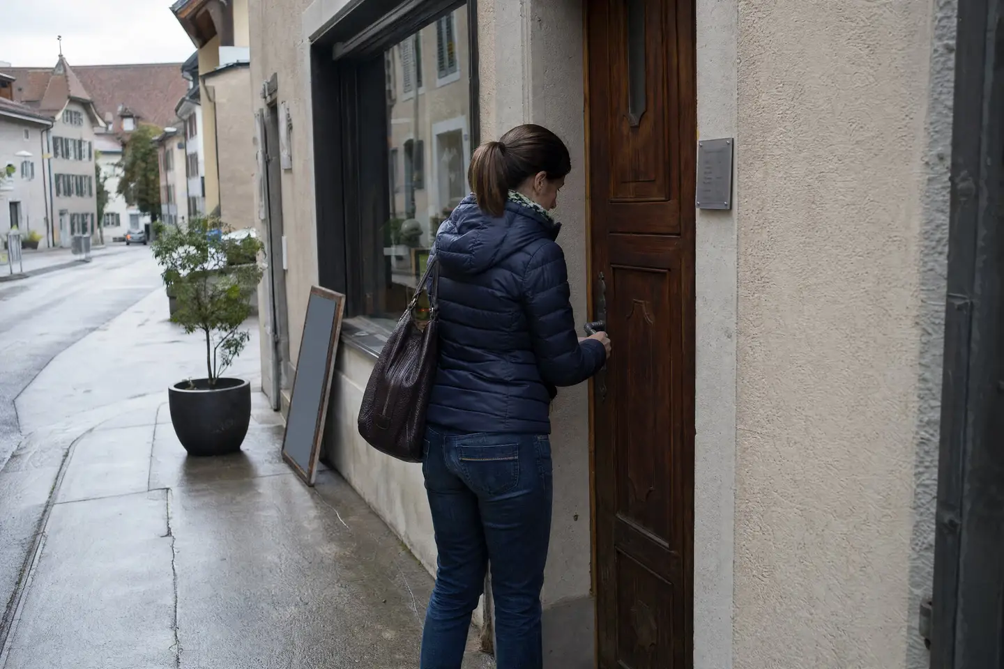 Ladeninhaberin schliesst am frühen Morgen die alte Holztür ihres Geschäfts auf, daneben ein Schild mit Öffnungszeiten