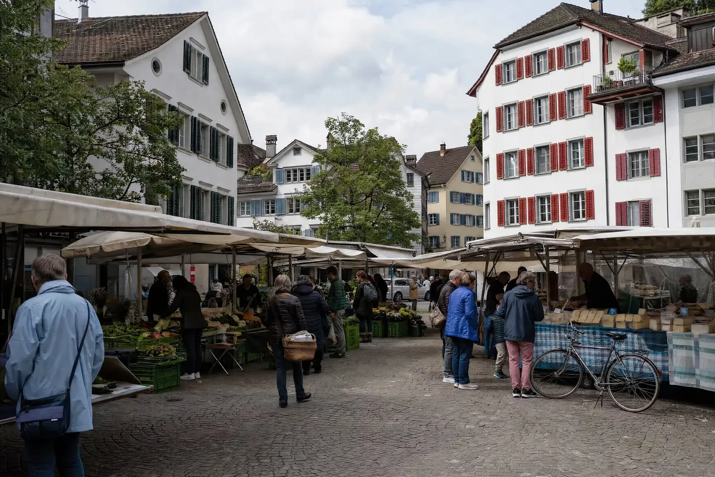 Wochenmarkt auf einem Altstadtplatz über Mittag, Stände mit Gemüse und Käse, Leute kaufen ein